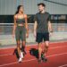 Sur l'image il y a deux personnes : un homme et une femme. Ils sont sur une piste d'athletisme et s'apprête vraisemblablement à débuter leurs footing avec leur tenue sportswear.