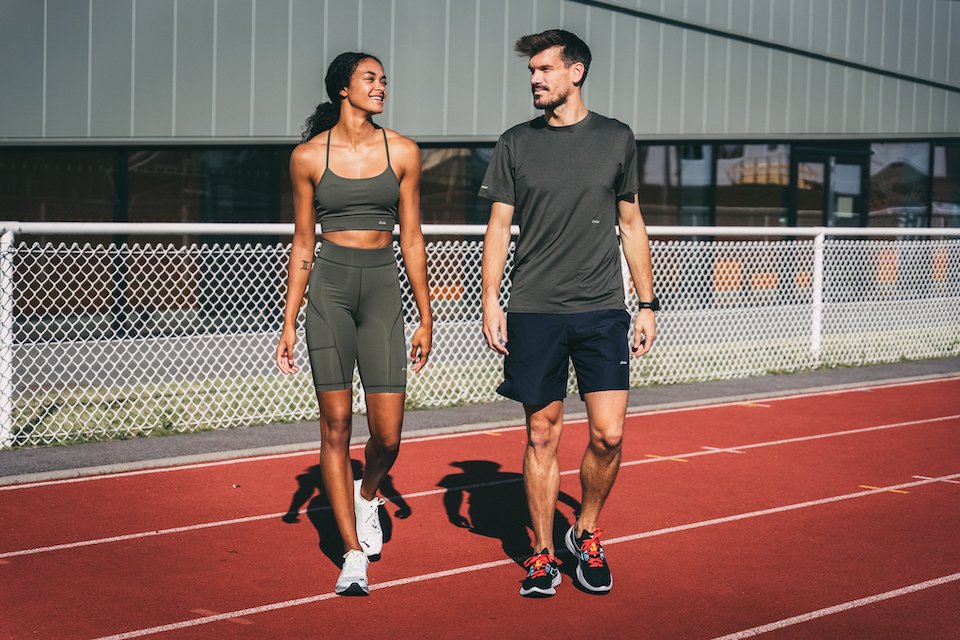 Sur l'image il y a deux personnes : un homme et une femme. Ils sont sur une piste d'athletisme et s'apprête vraisemblablement à débuter leurs footing avec leur tenue sportswear.